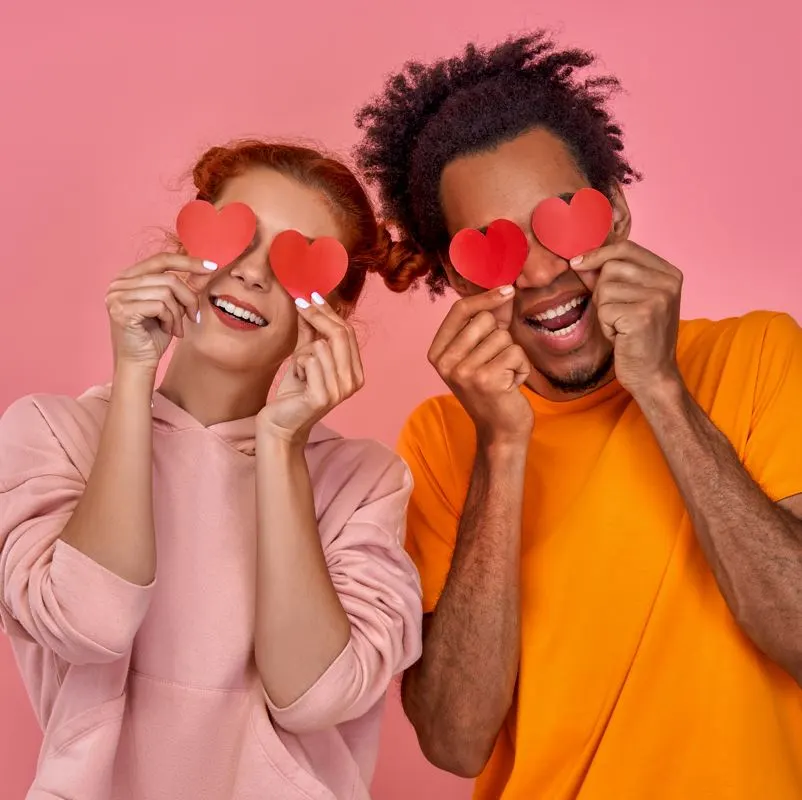 A young couple holding red hearts over their eyes