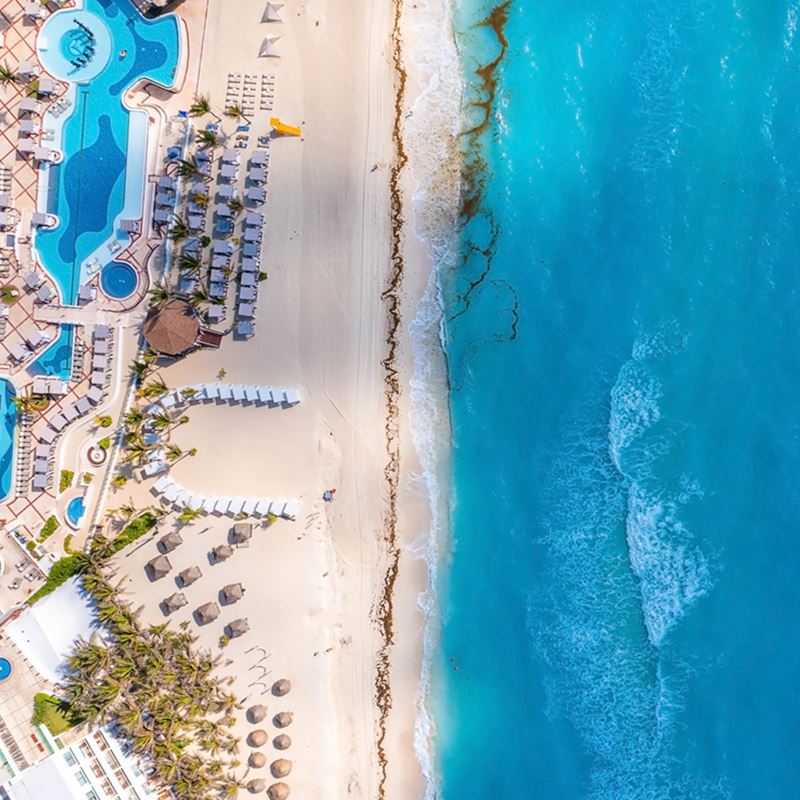 Aerial view of Cancun beach with resort, palm trees, palapas, and turqouise waters