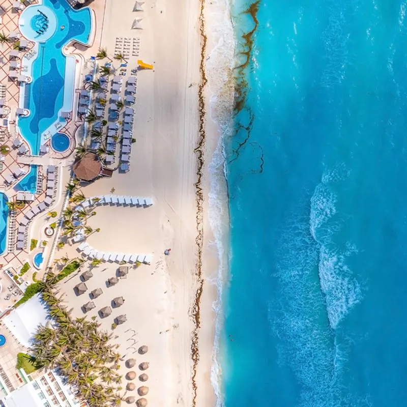 Aerial view of Cancun beach with resort, palm trees, palapas, and turqouise waters