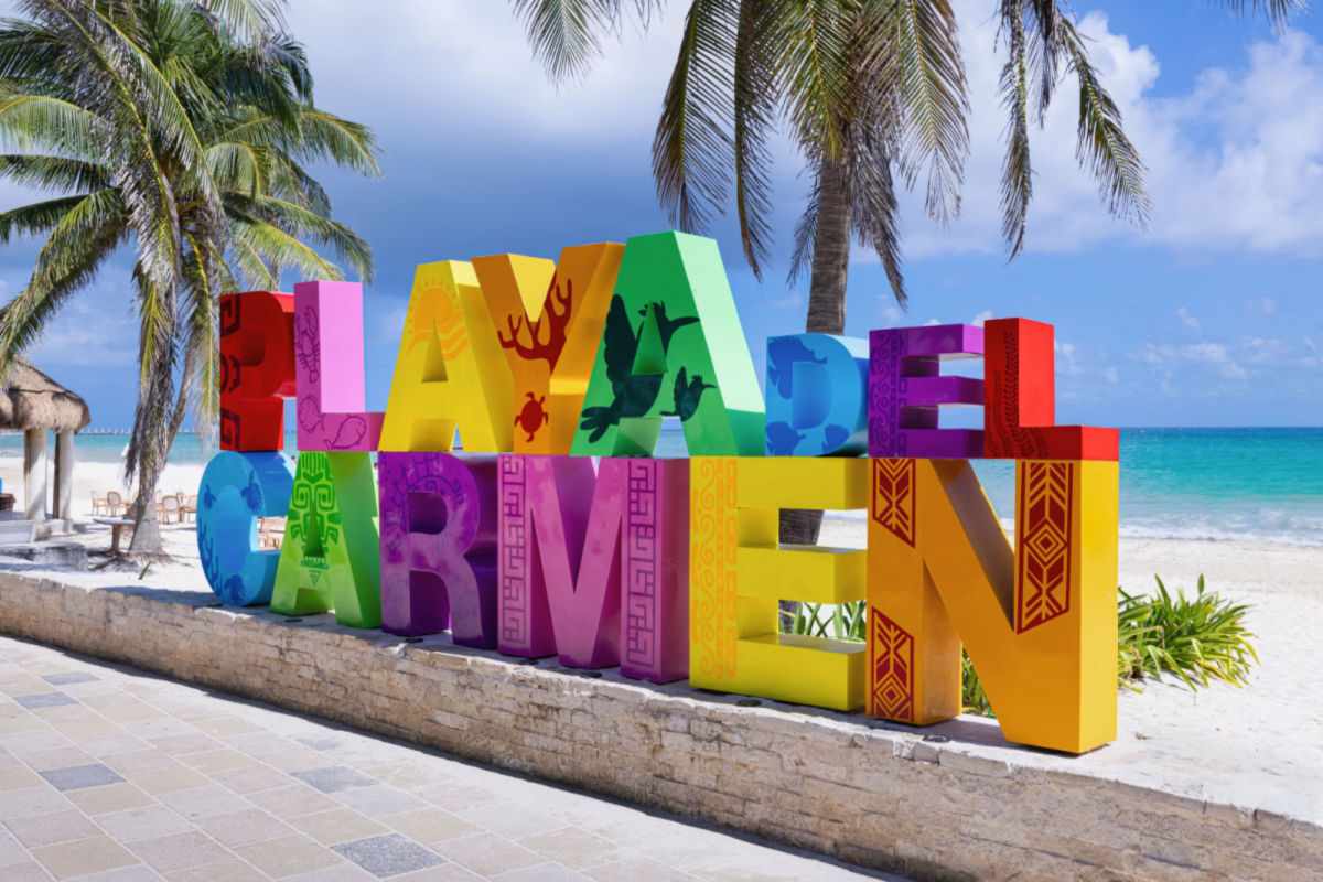 A colorful playa del carmen sign next to a beach