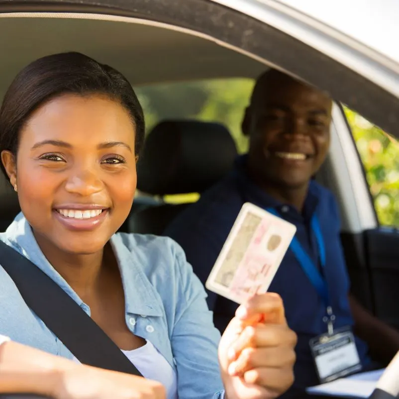 woman holding up a drivers license in a car on a sunny day