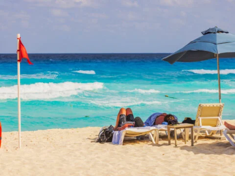 Cancun beach with a red flag flying in the wind and tourists lounging