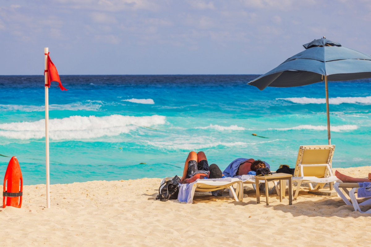 Cancun beach with a red flag flying in the wind and tourists lounging