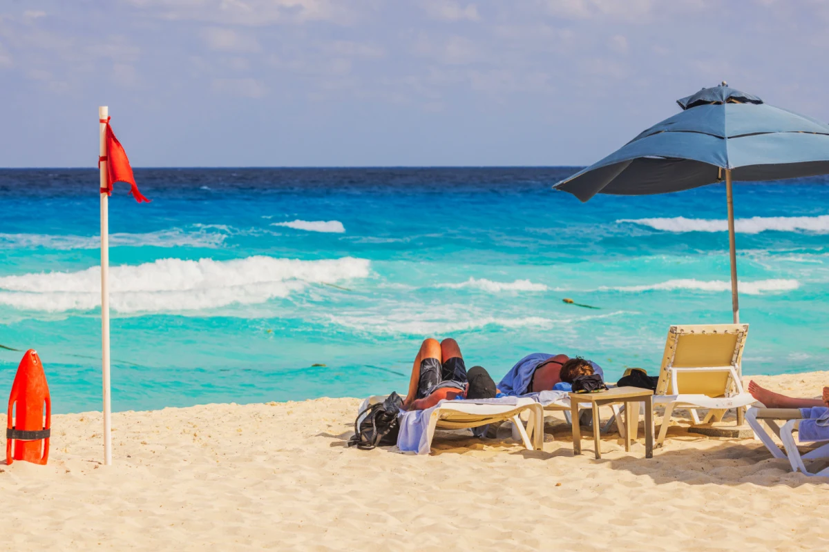 Cancun beach with a red flag flying in the wind and tourists lounging