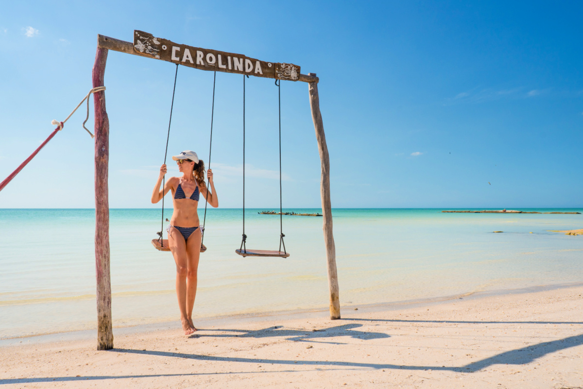 Girl with blue bikini sitting on a wooden swing in front of the Caribbean Sea on Holbox Island