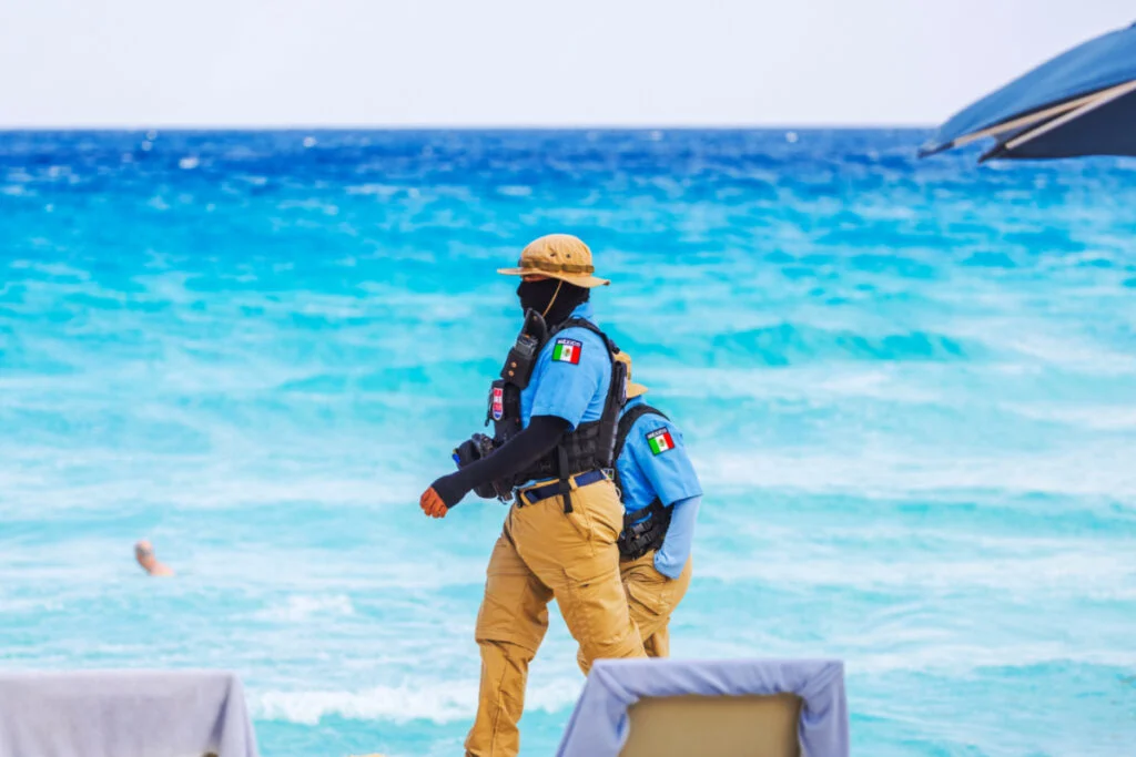 Police officers in tactical gear patrolling sandy beach near turquoise Caribbean sea. Cancun. Mexico.