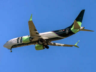 Calgary, Alberta, Canada. Oct 22, 2025. A vibrant Flair Airlines Boeing 737 MAX jet, in its distinctive green and black livery, soars through a clear blue sky, symbolizing modern discount travel.