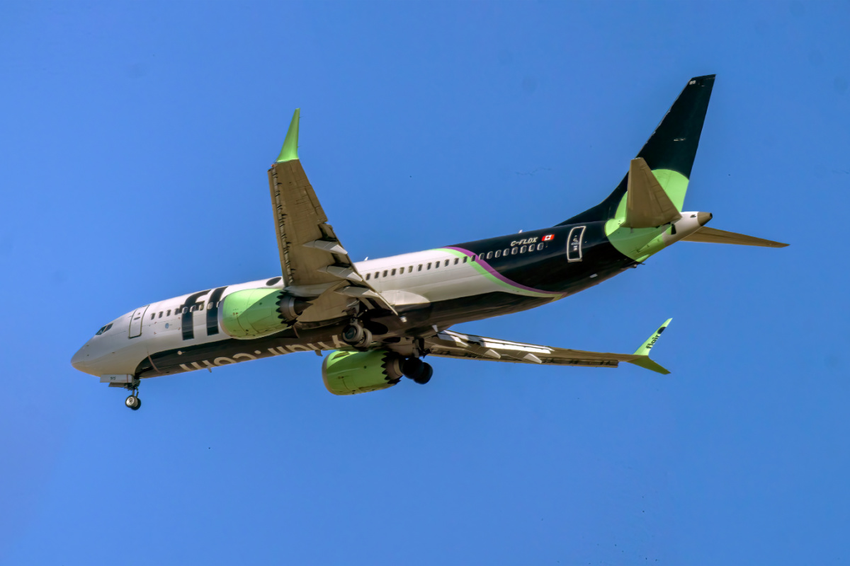 Calgary, Alberta, Canada. Oct 22, 2025. A vibrant Flair Airlines Boeing 737 MAX jet, in its distinctive green and black livery, soars through a clear blue sky, symbolizing modern discount travel.