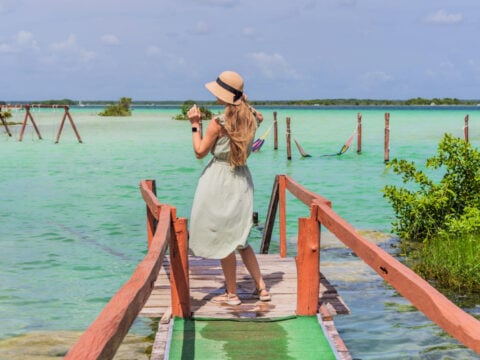 Mother with his toddler son exploring wooden pier over the turquoise waters of Bacalar Lake, Mexico. Peaceful tropical travel destination concept