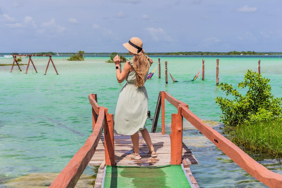 Mother with his toddler son exploring wooden pier over the turquoise waters of Bacalar Lake, Mexico. Peaceful tropical travel destination concept