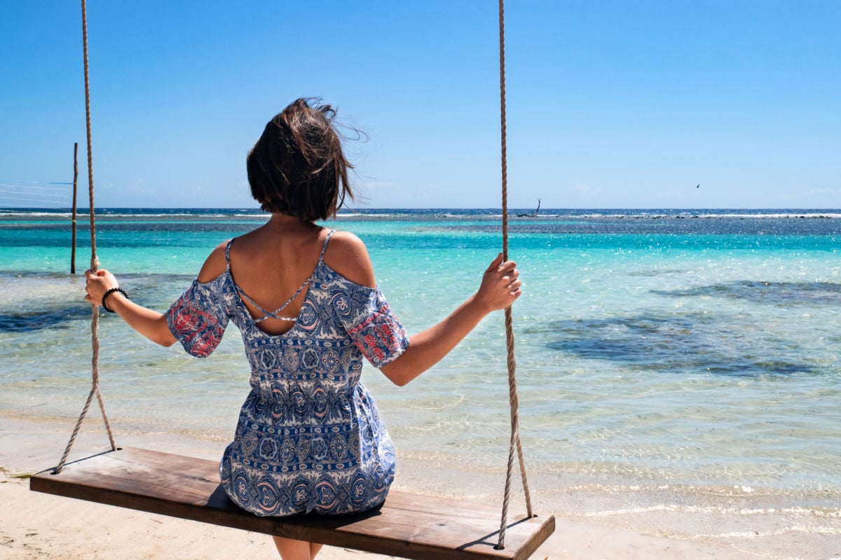 Young brunette girl lying on a swing at a paradise beach in the mexican coast, surrounded by white sand and turquoise water, at Mahahual village, in Quintana Roo, Mexico.