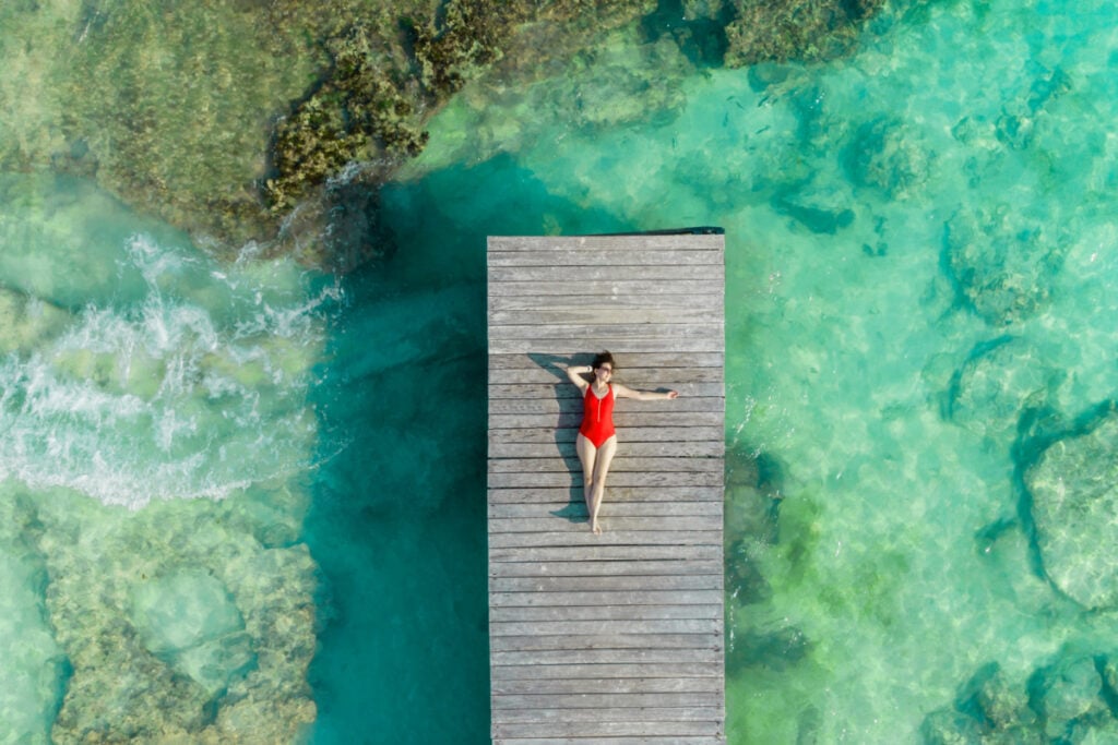 Aerial view of woman laying on wooden pier at sunny summer day in Cancun, Mexico, top view. Young woman wearing bright swimsuit in summertime in Caribbean. Summer beach vacation concept