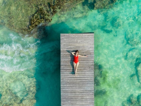 Aerial view of woman laying on wooden pier at sunny summer day in Cancun, Mexico, top view. Young woman wearing bright swimsuit in summertime in Caribbean. Summer beach vacation concept